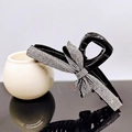 Dettaglio di un fermaglio per capelli nero con un fiocco decorato di strass - Strass Bianchi