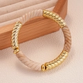 Dettaglio di maglie dorate a spirale e perline di resina marmorizzata su bracciale - Bianco Sporco