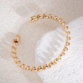 Détail macro d'un bracelet jonc torsadé doré posé sur une pierre texturée beige - Bracelet manchette ouvert à boule torsadée en spirale dorée