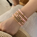 Stack of 10 layered pink clay and gold bead bracelets worn for a bohemian resort style - Pink
