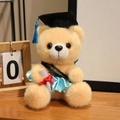Hellbrauner Abschluss-Teddybär mit Doktorhut und Glückwunschschärpe auf dem Schreibtisch - Hellbrauner Bär-Himmelblaue Kleidung / 18cm