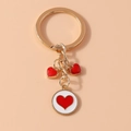 Detalle de un llavero de metal dorado con corazones esmaltados rojos y un colgante - Blanco Rojo