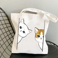 White canvas tote bag featuring two cute cartoon cats print resting on a black metal chair - Two Playing Cats