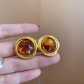 Detalle de pendientes de metal dorado con centro de resina ámbar sujetos con la mano - 14# Pin de Plata Oro Marrón Redondo