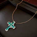 Macro shot of gold cross necklace featuring green zircon stones on textured background - Gold