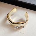 Macro del bracciale rigido dorato a onde irregolari su tessuto minimalista - Stile Onda Oro