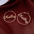 Detail van rosé gouden Kelly naam oorbellen op donkere fluwelen achtergrond - Goud