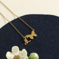 Gold butterfly necklace with Arabic letter pendant on elegant white leather surface - Gold L