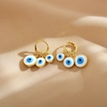 Boho-Ohrringe in Gold mit drei blauen Evil-Eye-Anhängern auf weichem Stoffhintergrund - Weiß