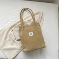 Fashionable camel corduroy tote bag with white patch detail on soft white bedding - Khaki