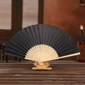Traditional black folding fan with bamboo frame and hollow carvings on a wooden base - Black