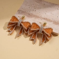 Detailopname van amberkleurige hars strik oorbellen met sprankelende witte steentjes erop - Strik Oorbellen / Bruin