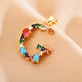 Macro view of gold letter G pendant with inlaid colorful gemstones on beige fabric - Letter G