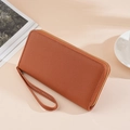 Brown lychee leather long wallet with wristlet strap and gold zipper on beige table - Litchi Pattern Long Light Brown