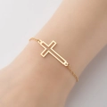 Primer plano detallado del colgante de cruz hueca en una pulsera minimalista de acero dorado - Dorado