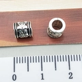 Silver Tibetan beads with star and maple leaf patterns displayed next to a ruler - Patterned Tube Spacer Bead