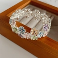Detail von bunten Emaille-Blumenanhängern an einem elastischen Armband auf Holztablett - Bunt