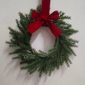 Mini Christmas wreath with green pine needles and a large red velvet bow hanging on a wall - Large Red Velvet Bow Wreath