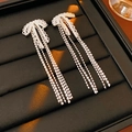 Macro shot of silver tassel bow earrings with sparkling zircons on a black leather tray - Silver Needle - Bowknot Tassel Style / Silver
