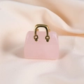 Close-up of pink crystal mini handbag pendant with a gold handle on beige fabric - Rose Quartz