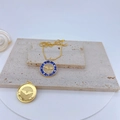 Detail of gold evil eye pendant with blue enamel and textured smiley charm on beige stones - Blue Enamel Eagle Round