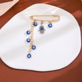 Gold Hamsa hand brooch with blue evil eye charms and tassels on a white ceramic tray - Tassel Evil Eye Style (Z103)