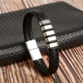 Close-up of black braided leather bracelet with silver metal charms on wood surface - Black