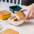 White square ceramic snack bowl with bamboo lid being opened on a textured tray - Replacement Bamboo Lid