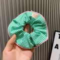 Green checkered hair scrunchie with pink edges and beige heart detail in hand - Small Grid / Green