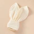 Detalle de mordedor de madera con suaves orejas de conejo de gasa en color crema suave - Blanco Roto