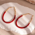 Detail of large oval red enamel drop earrings on a textured stone display - Gold+Red