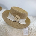 Dettaglio di cappello in paglia con fiocco ed etichetta UV su sfondo morbido bianco - Fiocco Beige