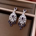 Macro shot of silver tassel earrings with purple drop stones on a dark velvet surface - Silver Purple