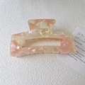 Detail view of a large square acetate hair claw clip with pink marble texture on paper - Pink White