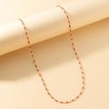 Detail view of a dainty gold necklace with vibrant red enamel beads on a beige prop - Gold Chain Red Enamel Beads