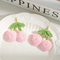 Detalle de pendientes de cereza rosa tejidos a mano en un plato de porcelana con relieve - Rosa