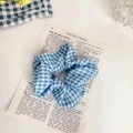 Blue and white gingham fabric scrunchie displayed on a vintage French pastoral background - Ocean Light Grid