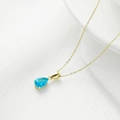 Elegante collar de titanio dorado con colgante de gota de agua azul sobre tela texturizada - Oro + Circonita Azul Aguamarina