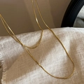 Gros plan du collier doré à double couche sur un fond de tissu texturé élégant - Chaîne Serpent Double Couche / Doré