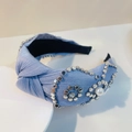 Detail eines blau gefalteten Knotenstirnbands mit silbernen Nieten und Perlenverzierung - Metallic-Blau