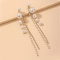 Détail de boucles d'oreilles pendantes asymétriques avec perles et strass sur fond beige - Tige d'oreille en argent - Boucles d'oreilles à franges dorées