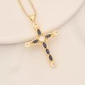 Macro detail of gold cross pendant with deep blue and clear gems on a white tray - Sapphire Blue