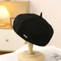 Dettaglio di basco vintage nero in lana con etichetta metallica su supporto di legno - Nero