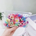 Primer plano de gomas de pelo de colores en bolsa con un adorno de flor margarita - Bolsa de Margaritas Pastel Claro