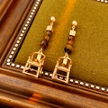 Detail von Vintage-Goldohrringen mit Stuhlanhänger und braunen Perlen auf grün - Gold & Kaffee