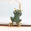 Detailed close-up of a vintage bronze frog brooch with green crystal rhinestones - Olive Green