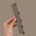 Detail eines gewellten Haarkamms mit fünf eleganten schwarzen Kamelienblüten-Akzenten - Kamelienmuster