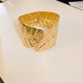 Wide gold metal bangle featuring embossed leaf vein texture and a hinged clasp - Gold