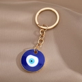 Detailaufnahme des goldenen Schlüsselanhängers mit blauem Evil Eye Anhänger auf braunem Stoff - Gold Dunkelblau Rundes Auge