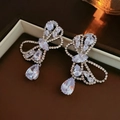 Silver bow earrings with pear-shaped rhinestones on a brown jewelry box background - 925 Sterling Silver Earring Post - Zircon Hollow Bowknot Water Drop Tassel Studs
